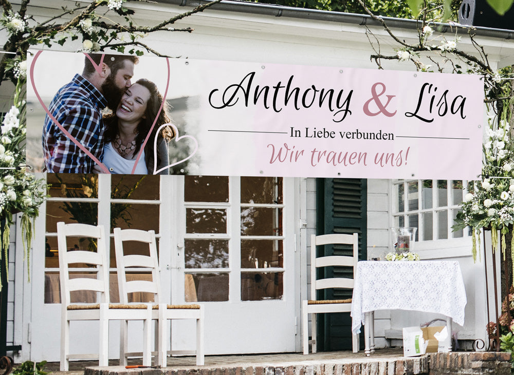 Romantisches Hochzeitsbanner mit den Namen Anthony & Lisa, verziert mit Herzmotiv und dem Schriftzug "In Liebe verbunden – Wir trauen uns!", stilvoll dekoriert für eine Hochzeitsfeier im Freien.
