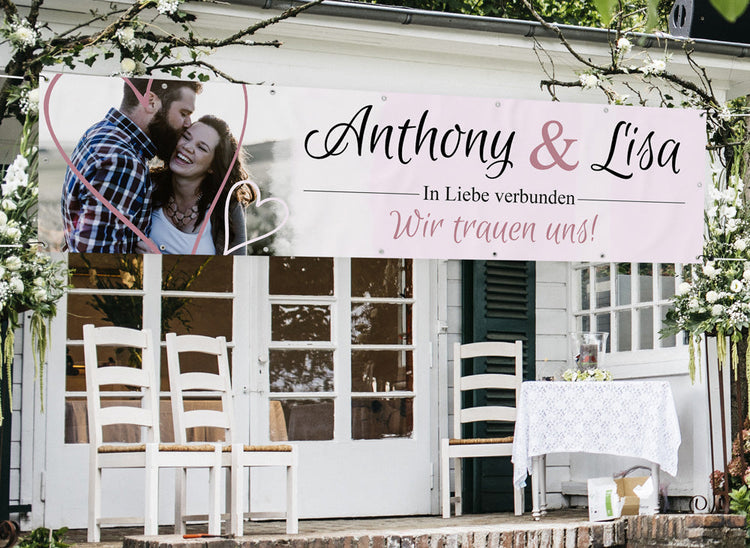 Romantisches Hochzeitsbanner mit den Namen Anthony & Lisa, verziert mit Herzmotiv und dem Schriftzug "In Liebe verbunden – Wir trauen uns!", stilvoll dekoriert für eine Hochzeitsfeier im Freien.