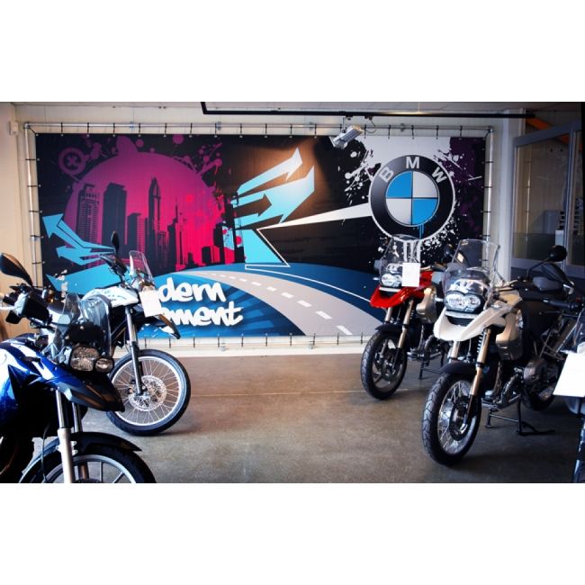 BMW-Motorrad-Showroom mit mehreren Adventure-Bikes vor einer farbenfrohen Wandgestaltung. Das große Banner im Hintergrund zeigt eine stilisierte Straße, eine Skyline und das BMW-Logo mit dem Schriftzug 'modern movement'. Die Motorräder sind in verschiedenen Farben ausgestellt und bereit für den Verkauf oder die Präsentation.