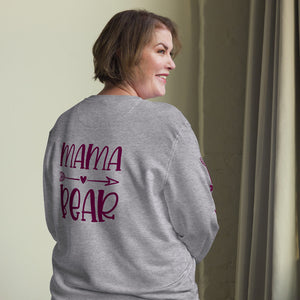 Frau mit grauem Pullover, auf dessen Rückseite 'Mama Bear' in einer verspielten Schrift mit einem Herz-Pfeil-Design steht. Perfekt für stolze Mütter.