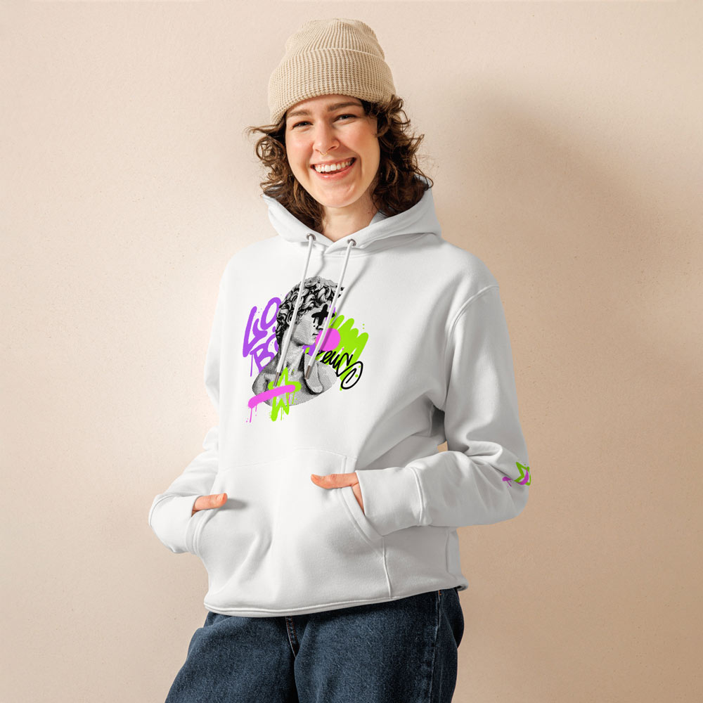 Eine lachende Frau trägt einen weißen Hoodie mit einem individuell bedruckten Design in Graffiti-Optik. Der Hoodie zeigt eine kreative Illustration mit Neonfarben und Schriftzügen. Sie kombiniert ihn mit einer beigen Strickmütze und einer lockeren Jeans für einen entspannten, modernen Look. Perfekt für trendbewusste Streetwear-Liebhaber.