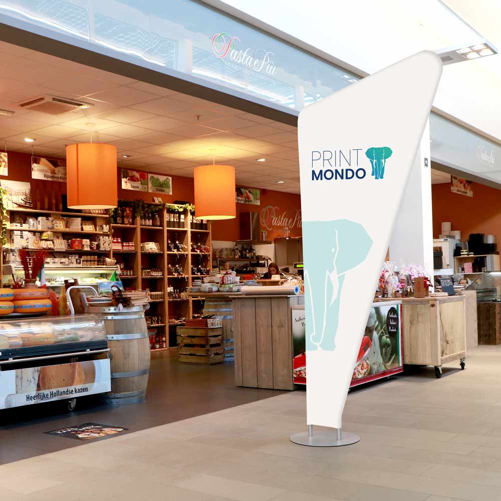 Bannerdisplay Triangel im Einsatz vor einem Geschäft. Hier mit Beispieldruck in weiss, türkis und blau mit dem Print Mondo Elefanten Logo.