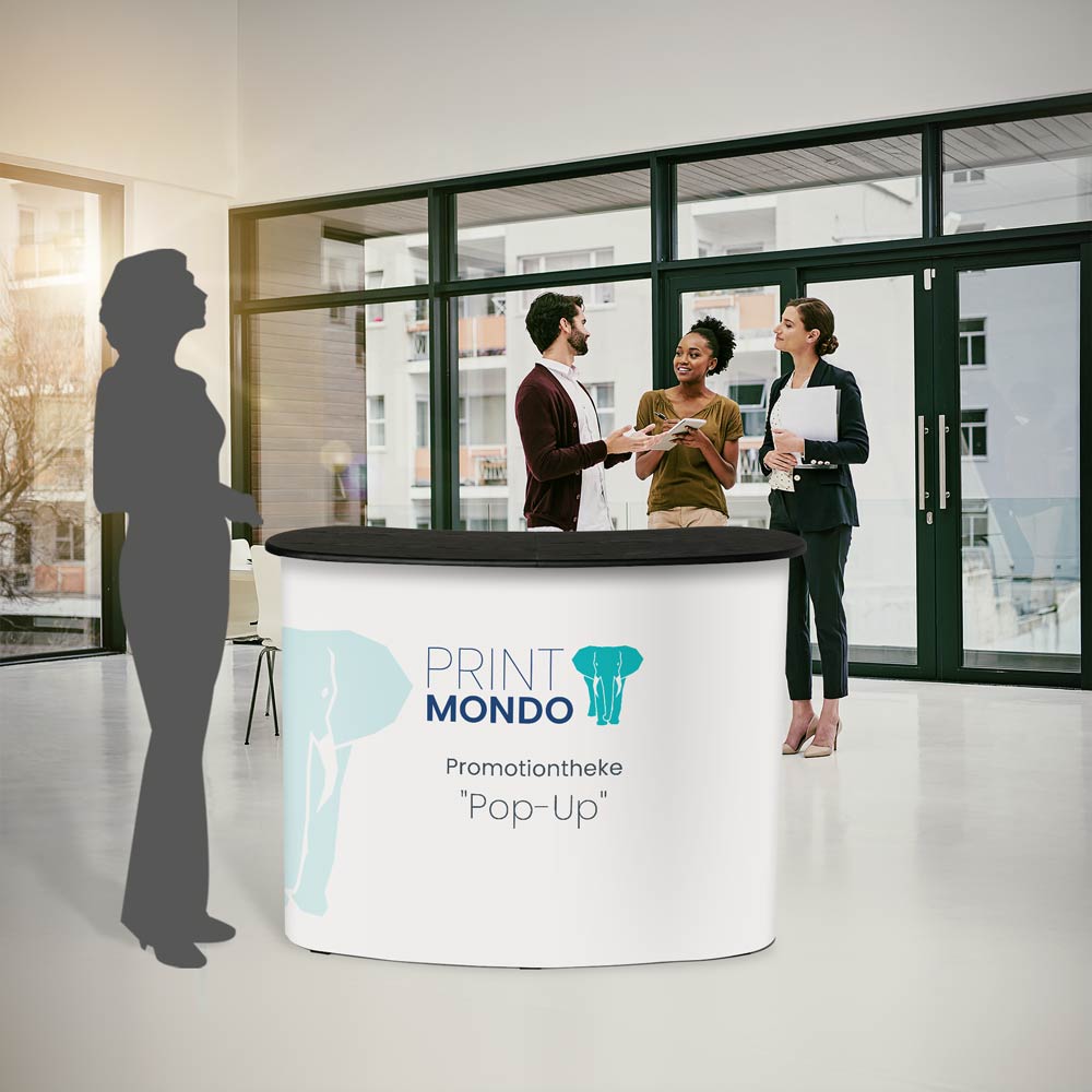 Promotiontheke mit schwarzer Tischplatte als Beispiel im Einsatz im Büro mit Schattenperson daneben zum Größenvergleich. Hier mit Beispieldruck in weiss, türkis und blau mit dem Print Mondo Elefanten Logo.