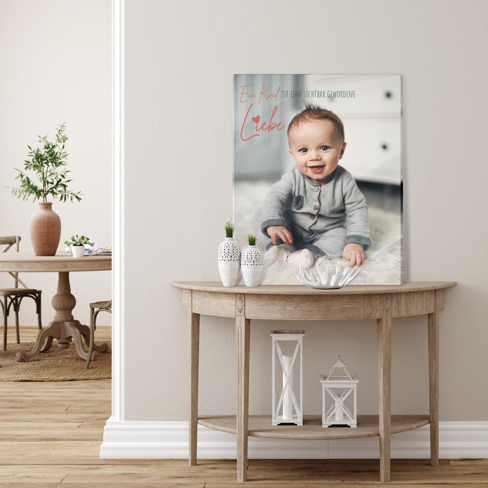 Acrylglasbild mit Babyfoto und Zitat „Ein Kind ist eine sichtbar gewordene Liebe“, dekorativ auf einem Tisch im Wohnzimmer platziert.